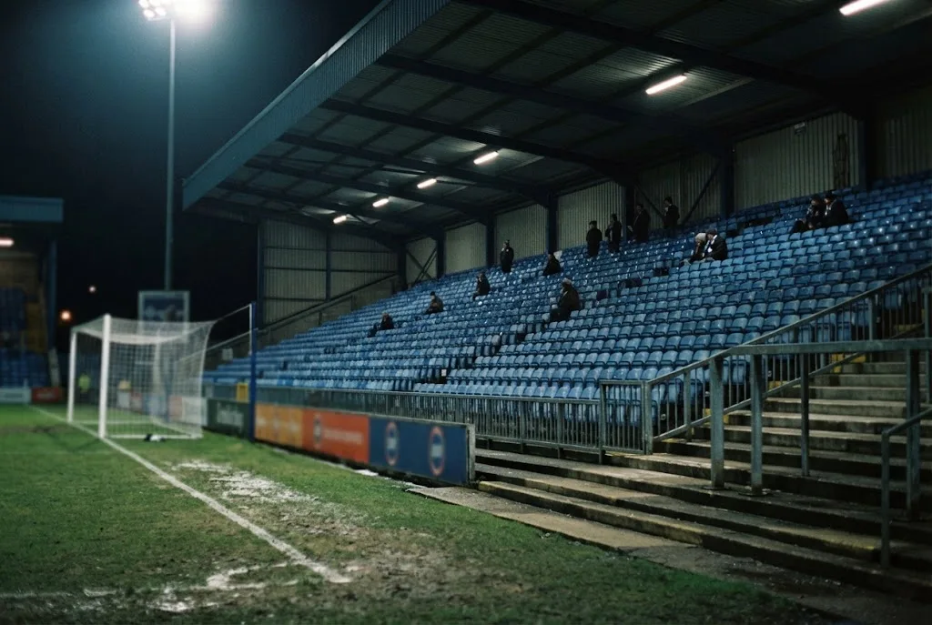 An almost empty stand behind a floodlit goal on a midweek evening
