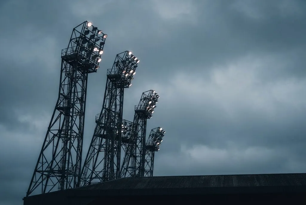 Floodlight pylons rising above a stadium roof against an overcast evening sky