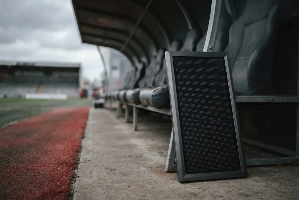 A numbered substitution board resting against an empty dugout bench